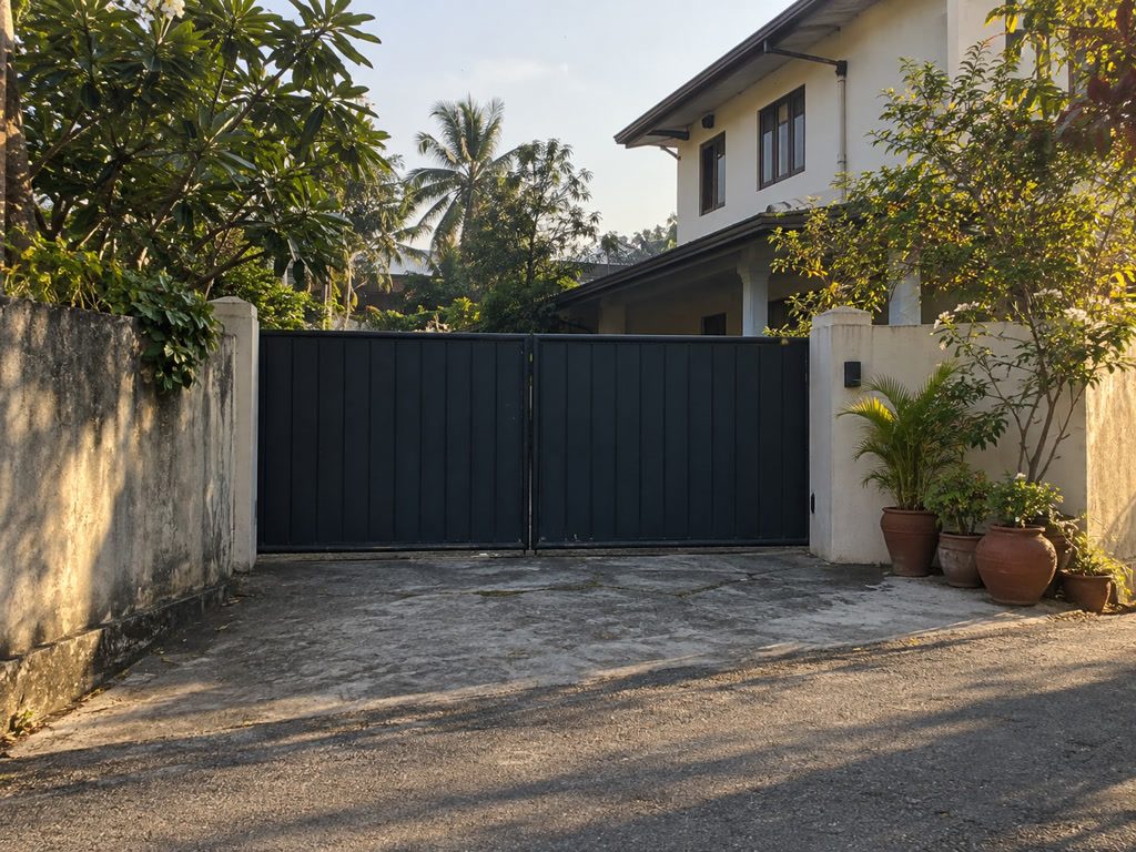 Gated house driveway with laterite-red pots, empty of people